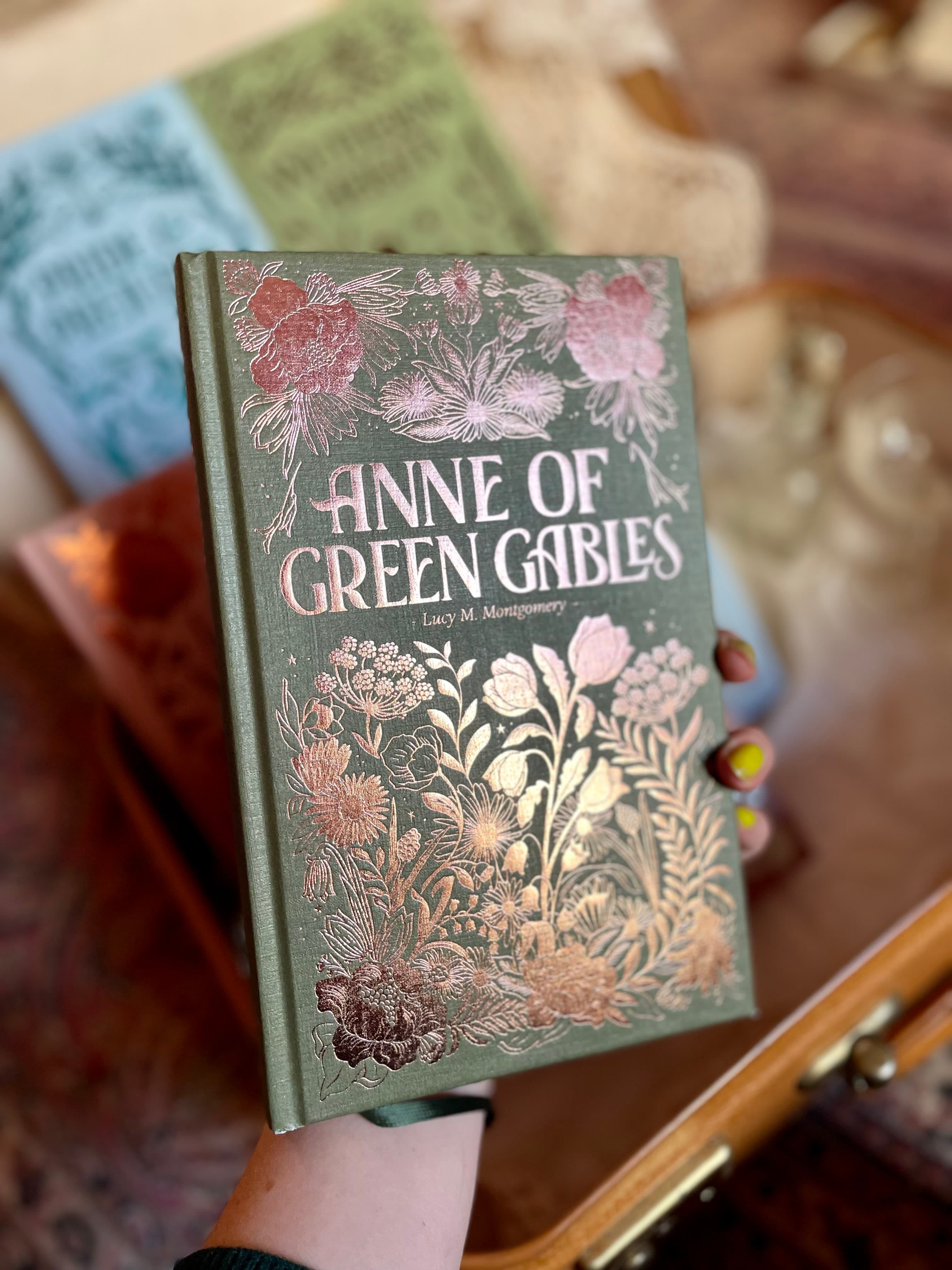 Main tenant un livre avec une couverture illustrée très dense à motifs floraux pour une édition spéciale d'Anne aux pignons verts.