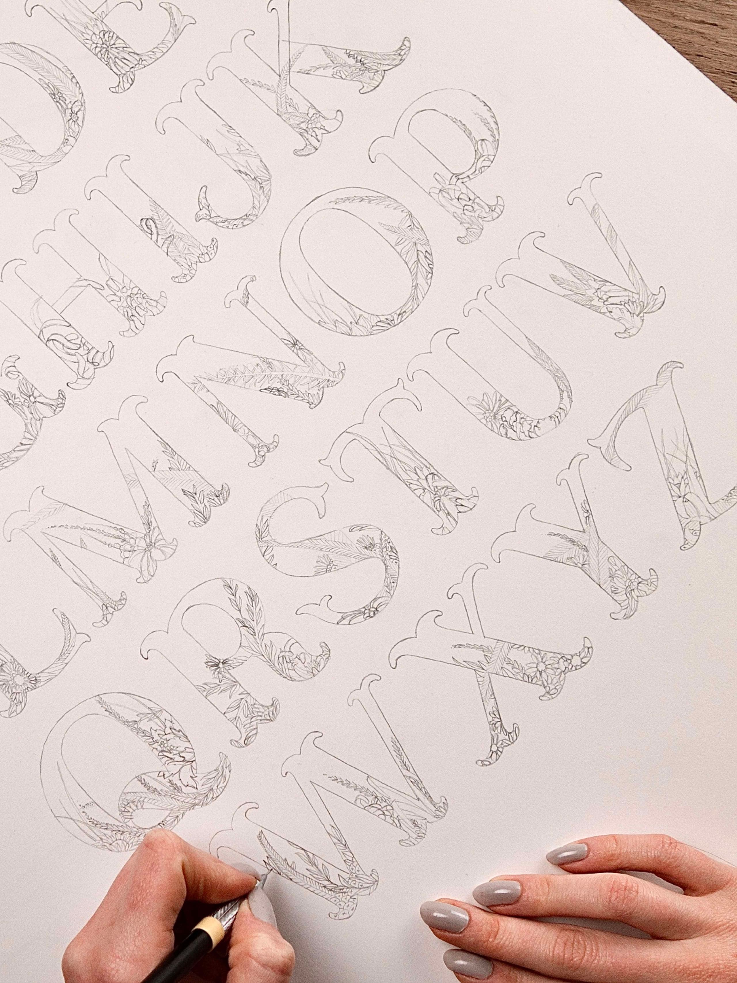 Gros plan de mains utilisant un crayon pour esquisser des détails floraux complexes sur une lettre en papier.