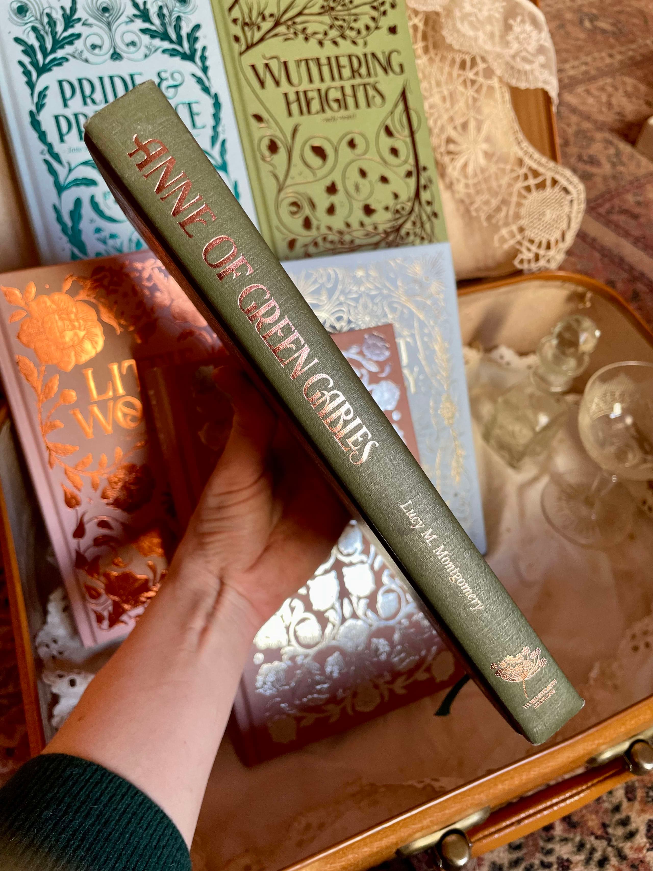 Gros plan du dos d'un livre orné de motifs botaniques délicats et du titre Anne aux pignons verts.